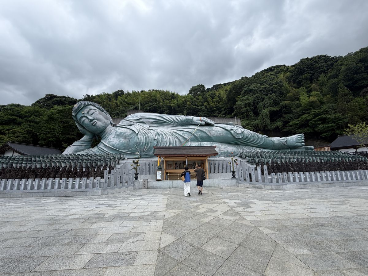 南蔵院の釈迦涅槃像。曇り空の下、背後に緑の山が迫る
