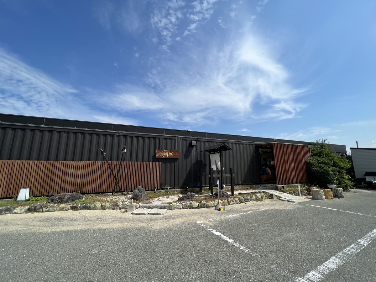 鮨屋台 岡垣総本店の外観。黒い金属壁と焼き板の腰板、青空