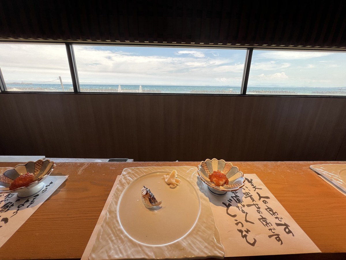 菊の形の小鉢に盛られたいくらと、窓の外の海